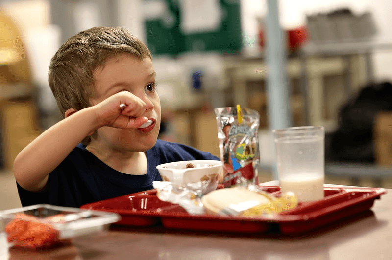 Young boy eating a tray lunch.