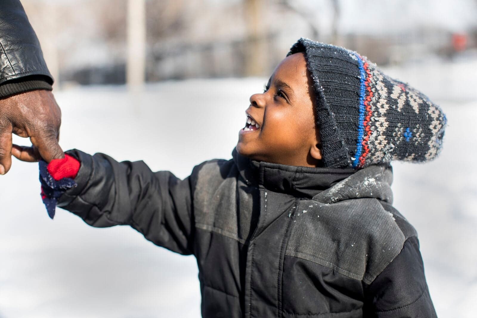 Little boy bundled up in winter gear holding hands and smiling.